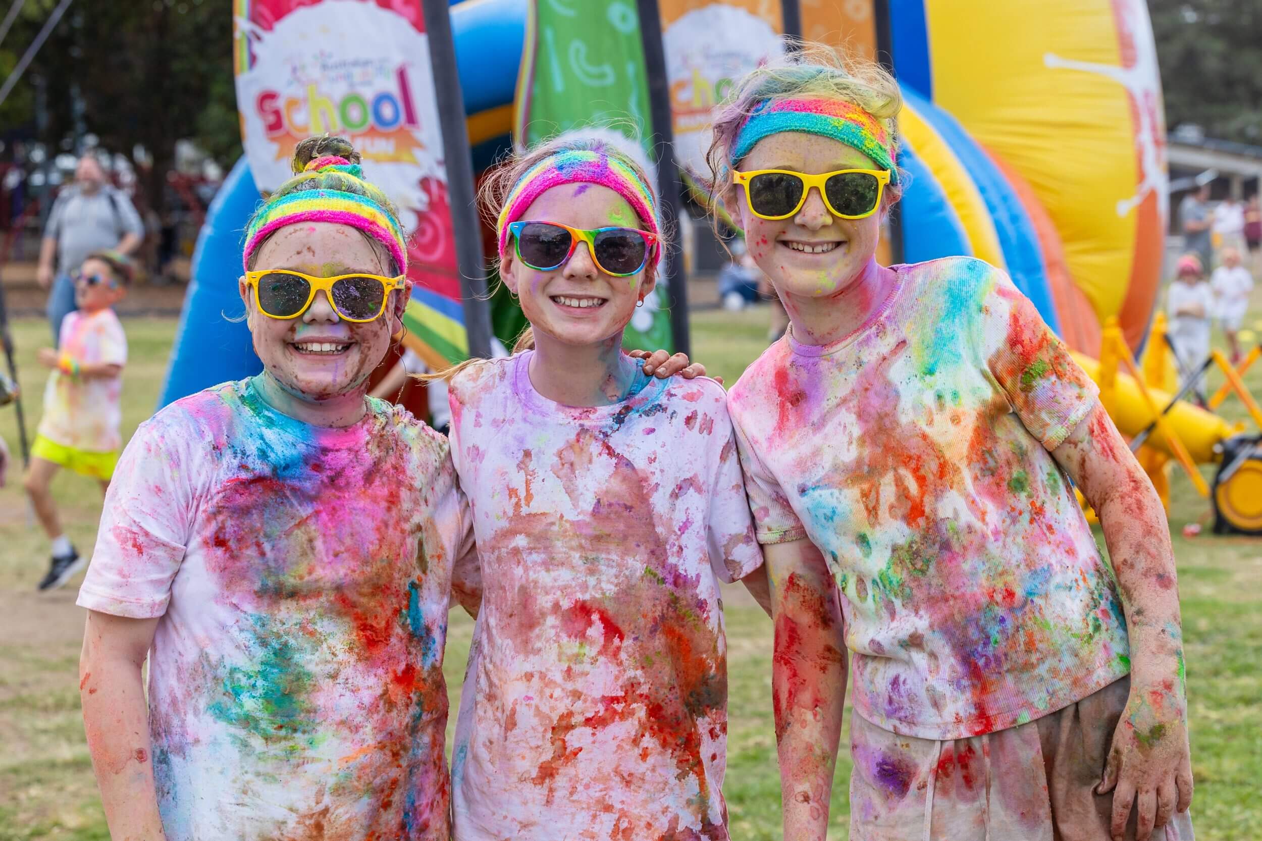 three children smile at the camera, covered in colour after enjoying a school fun run.