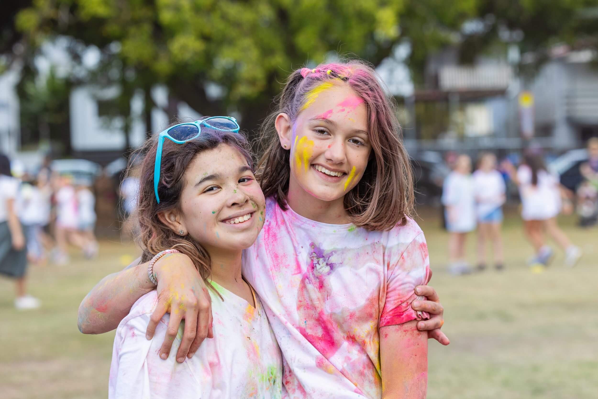 Children smile at the camera covered in coloured powder after completing a successful colour fun run. 