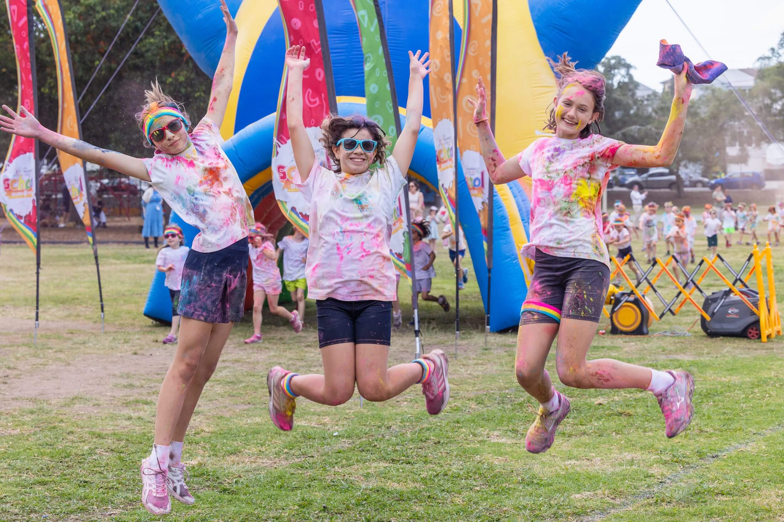 three children jump for job covered in colour after completing a school colour fun run.