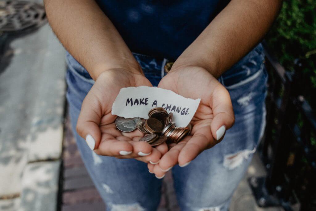two hands holding coins and a piece of paper reading"make a change"